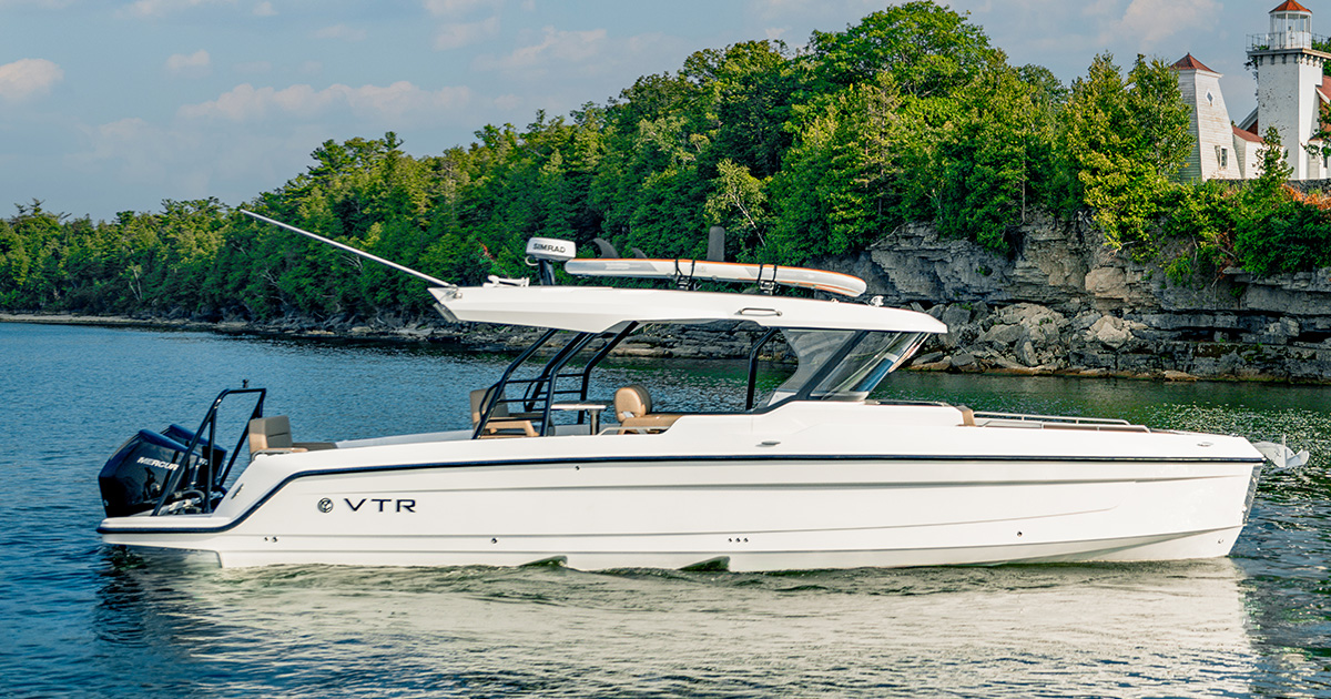 A 38 VTR ventures through water near a rocky shoreline with dense green trees.